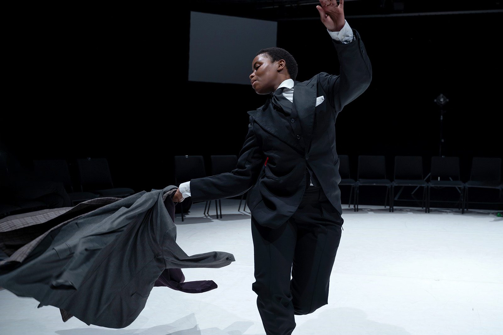 Person in einem dunklen Anzug hat einen anderen Anzug in der Hand und schwingt ihn in einer Pose umher.